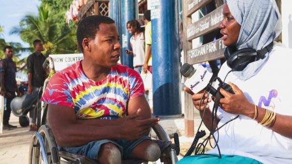 A woman interviews a man in a wheelchair who has amputated legs.