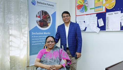 A women sitting in a wheelchair with a man smiling standing besides her.