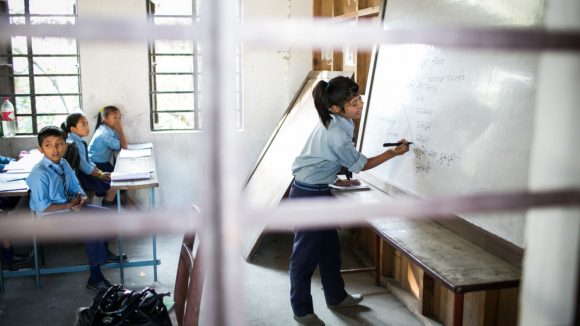 A girl writes on a whiteboard in a classroom.