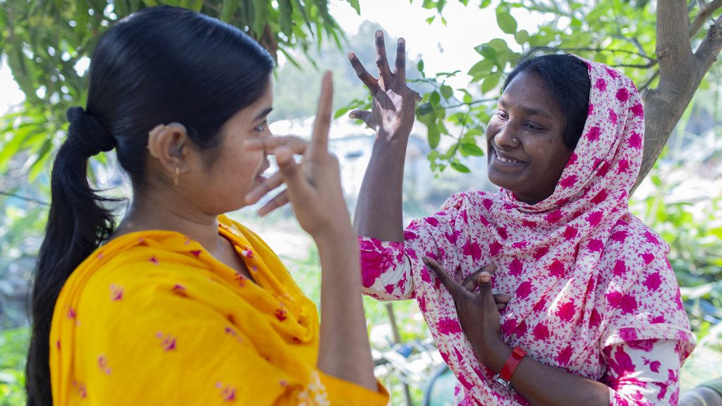 Two women in Bangladesh communicating using hand gestures.