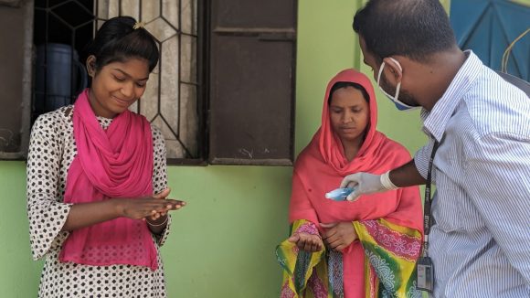 Three people in Bangladesh use hand sanitiser.
