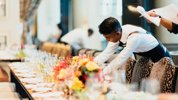 A hotel worker arranges a dinner table.