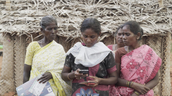 Three women stand together looking at a mobile phone.