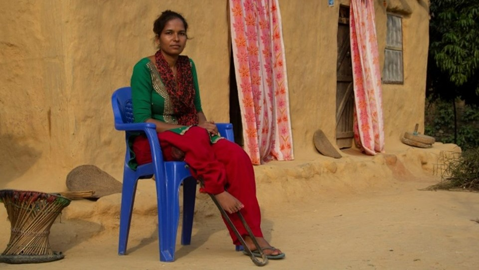 Durga, from Nepal, sits in a blue plastic chair outside her home in Nepal. She was afflicted with polio when she was a child and uses an assistive device to help her walk.