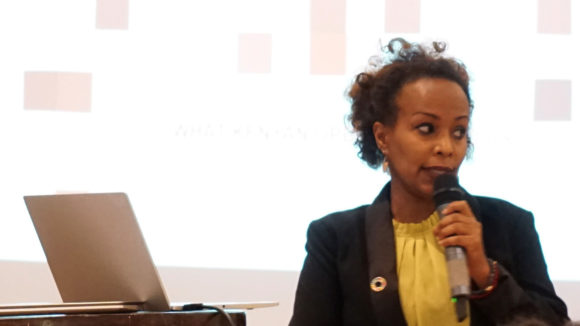 Martha Bekele stands during a presentation with a microphone in her hand.
