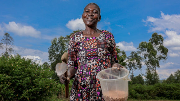 A woman farmer is photographed on her land holding farming tools and seeds.