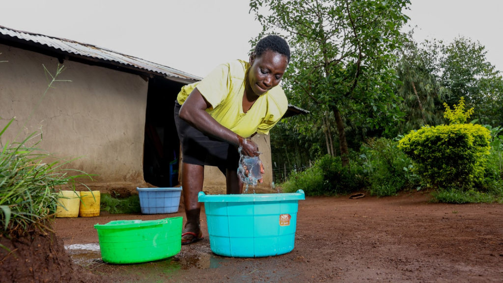 Maren, a sorghum farmer, washes items in a bucket outside her home.