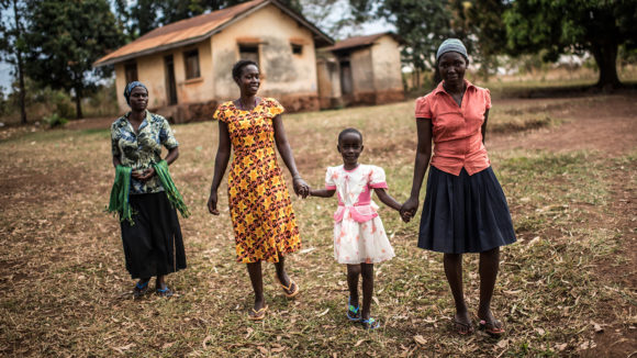A group of women and girls linking hands and smiling in a remote village in Uganda.