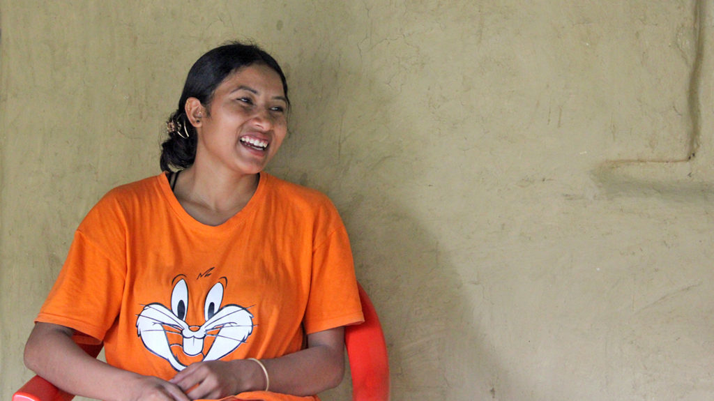 A woman wearing a bright orange t-shirt smiles broadly.
