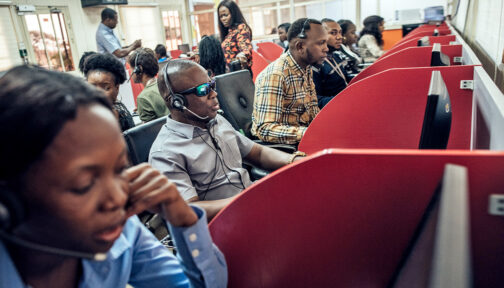 Staff members in an office in Lagos, Nigeria. They're wearing telephone headsets. One man is wearing dark glasses.