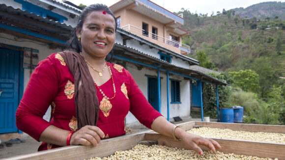 A woman stands outside in front of a large crate of coffee beans.