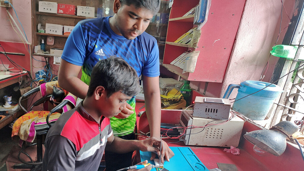 A man shows a young person how to solder some electrical equipment.