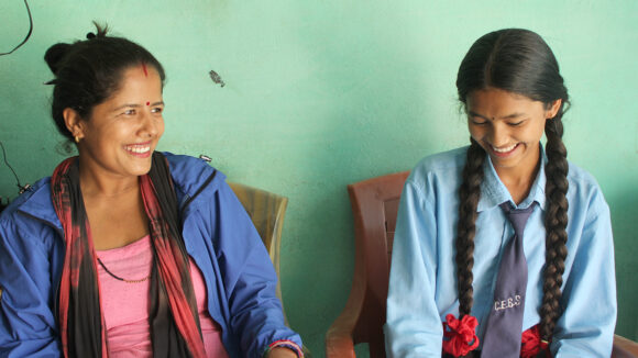 A woman and girl smile together while sitting inside.