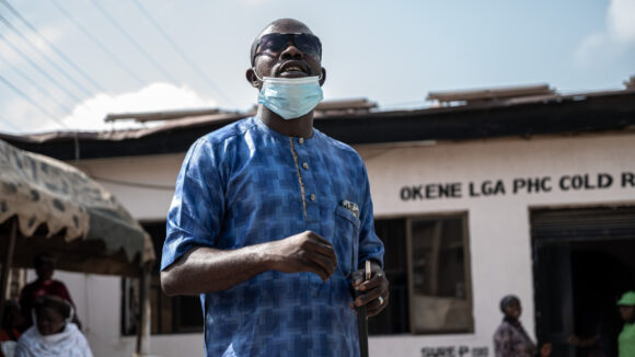A man wearing a blue shirt and dark glasses is standing outside a health centre.