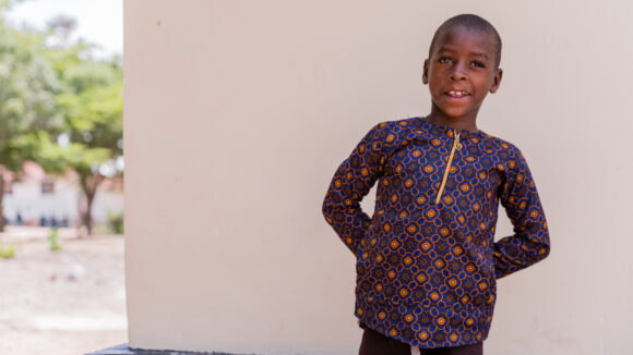 A young boy wearing a patterned shirt smiles for the camera.