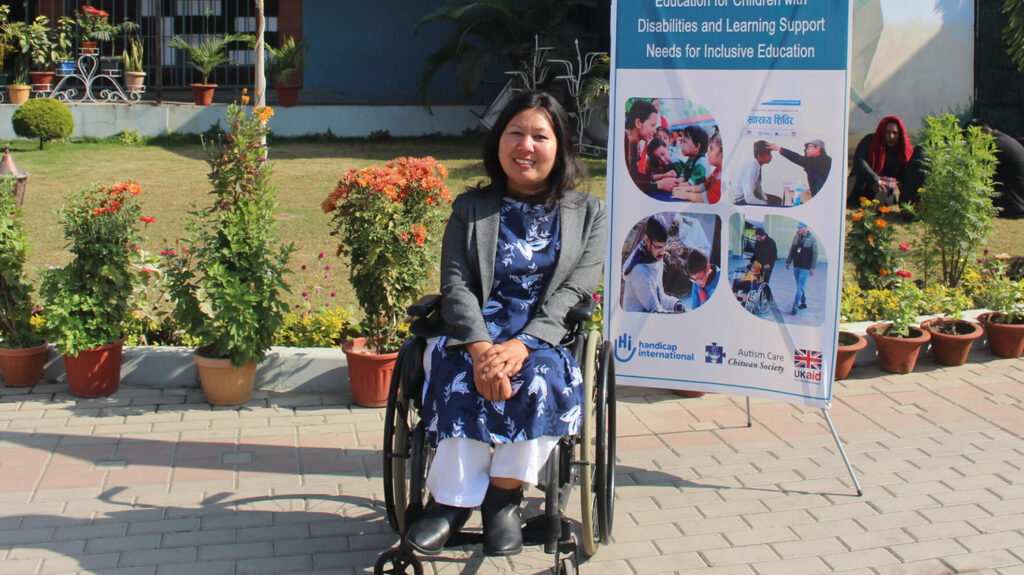 A woman on a wheelchair outdoors and smiling at the camera