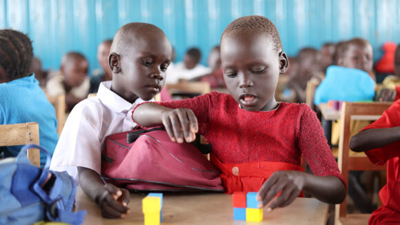 A girl and a boy are playing with coloured blocks in a classroom.