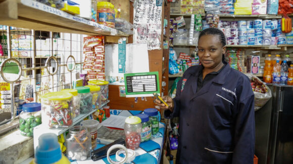 A female retailer is photographed in her shop, holding a smart phone.