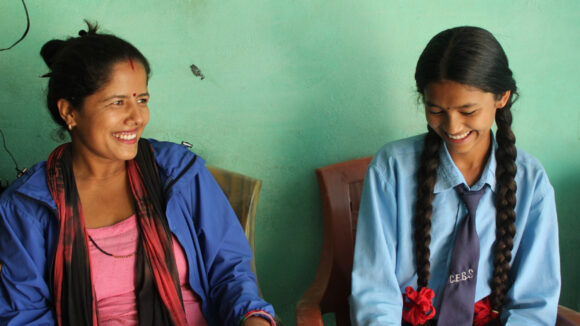 A woman sits next to a girl wearing a school uniform at a youth club in Nepal.