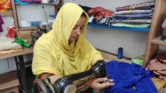 A girl wearing a yellow headscarf is using a sewing machine.