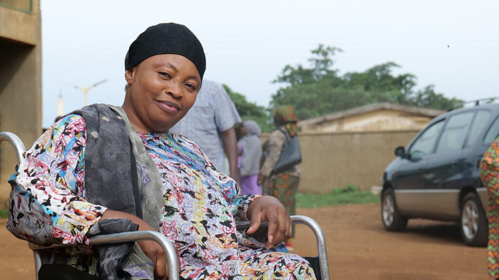 Risikat sits in her wheelchair in a car park.