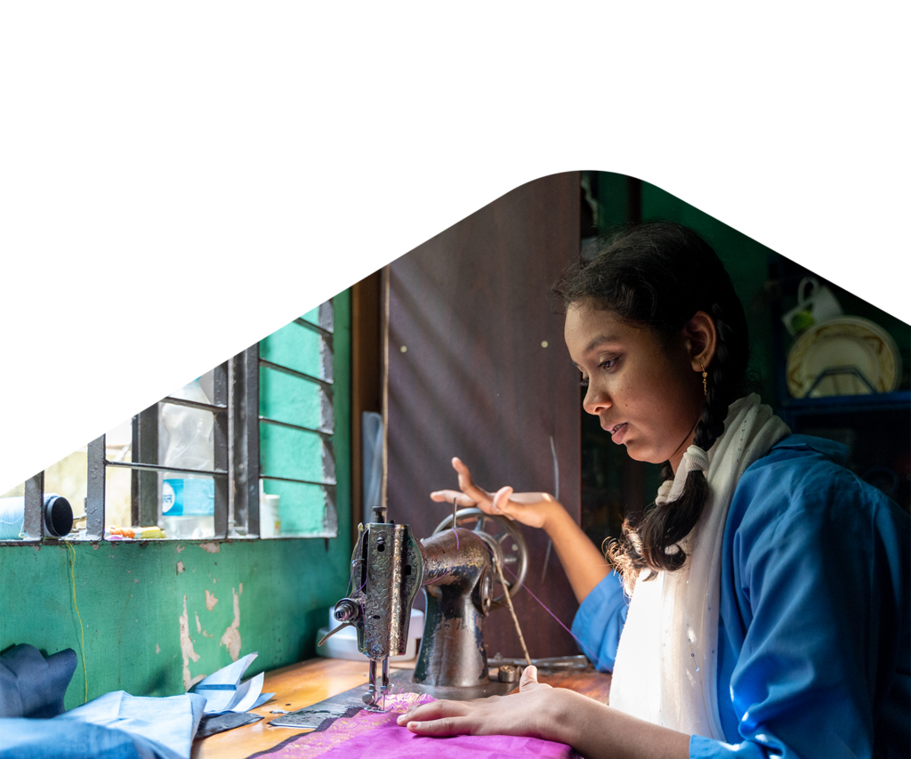 Mimi sits opposite a window using a sewing machine. She has a physical disability which affects her hands.