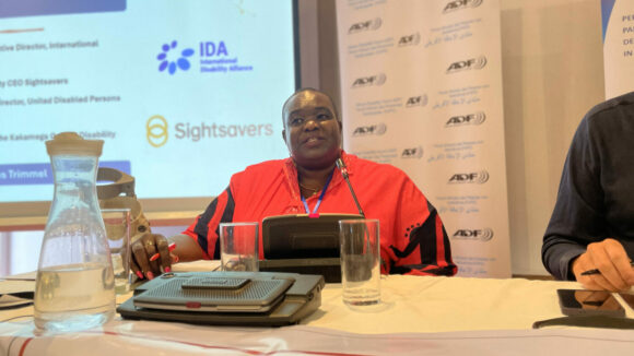 Lucy Mulombii speaks into a microphone during a panel session at the African Disability Forum conference.