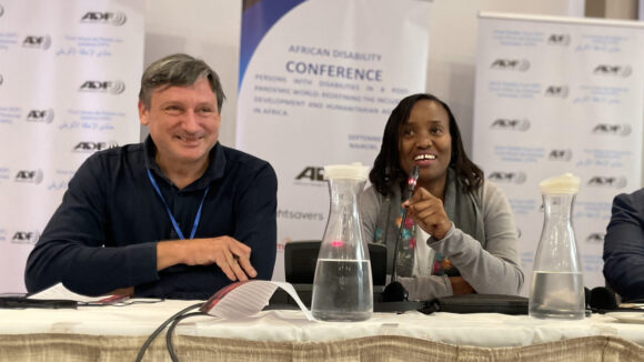 Sally Nduta speaks into a microphone. She is sitting next to Johannes, who is also a panel speaker.