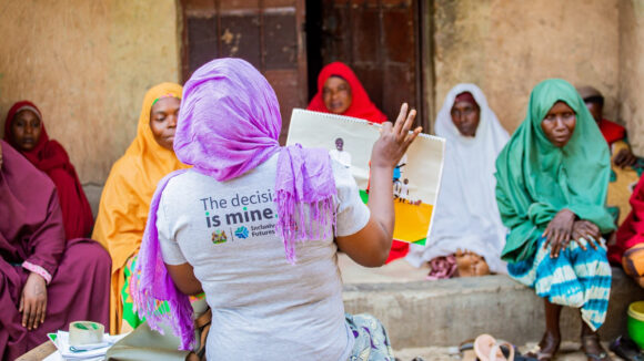 A woman wearing a grey T-shirt with the words 'The decision is mine' leads a workshop with other women with disabilities in a courtyard in Nigeria.