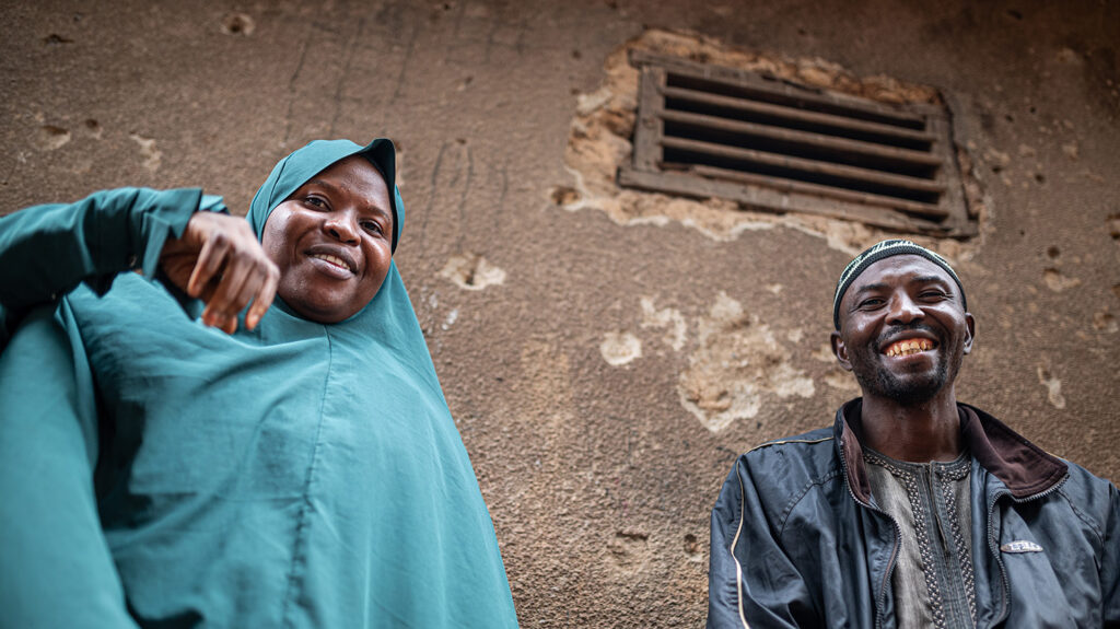 A woman wearing a hijab sits next to a man. They are both smiling.